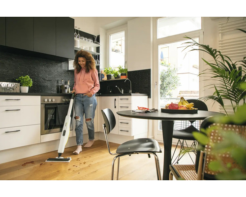Femme nettoie un plancher en bois dans une cuisine lumineuse avec un nettoyant pour sols durs