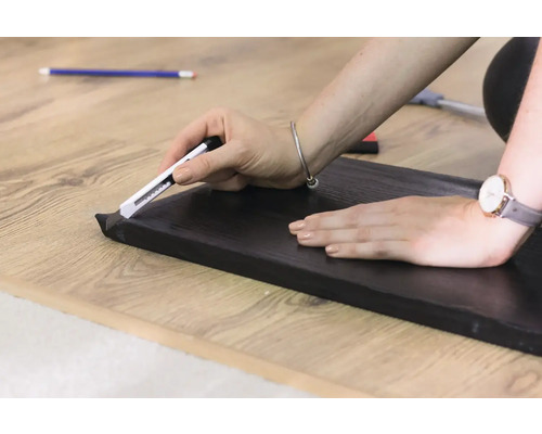 Zuschneiden einer Sockelleiste mit einem Cuttermesser auf einem Holzboden.