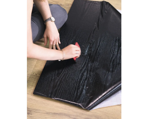 Eine Person verarbeitet eine selbstklebende Möbelfolie in Holzoptik mit einem Rakel.