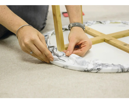 Gros plan d''une personne retirant le matériel d''emballage d''une table ronde avec des pieds en bois.