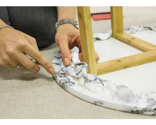 Une personne coupe le film d''une table ronde avec des pieds en bambou à l''aide d''un couteau