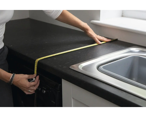 Une personne mesure un plan de travail de cuisine avec un mètre ruban.