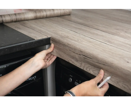 Personne collant un plan de travail avec un film décoratif aspect bois