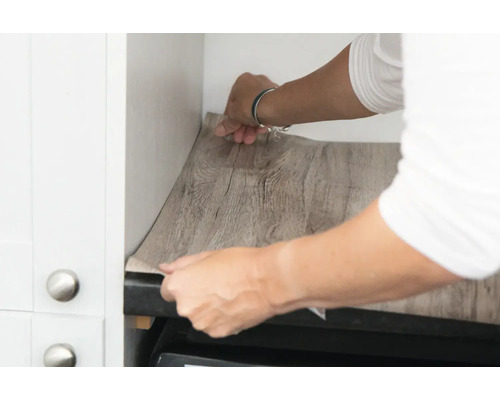 Une personne pose un film pour meubles imitation bois dans une cuisine.