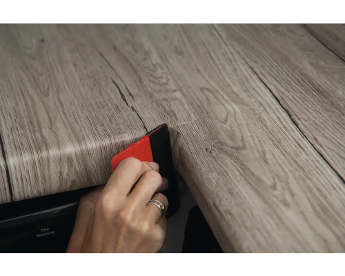 Une personne applique un film décoratif en bois avec une raclette