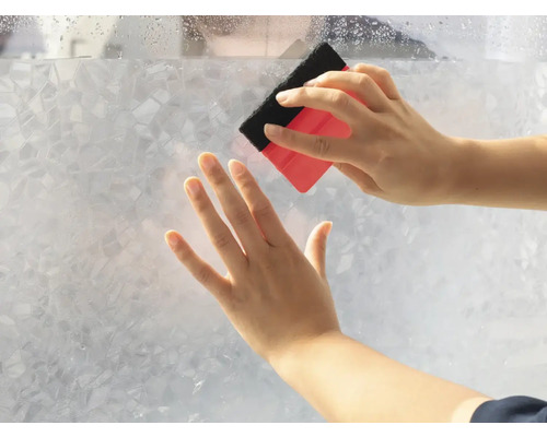 Une personne applique un film de protection visuelle avec une raclette sur une vitre
