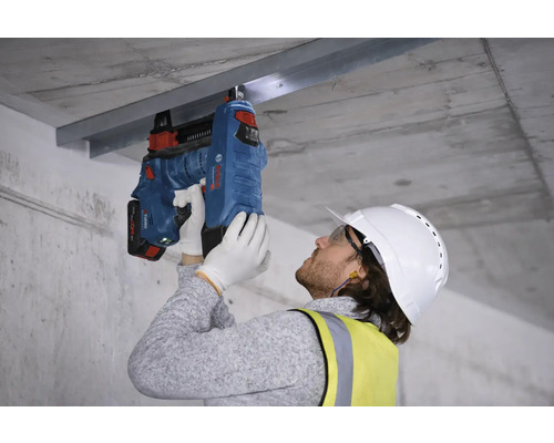 Ein Mann mit Schutzhelm befestigt eine Metallschiene mit einem Bolzensetzgerät an einer Betondecke.