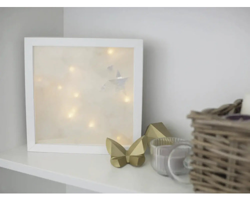 Dekorative Szene mit beleuchtetem Bilderrahmen, Zierfiguren und Korb auf einem Regal