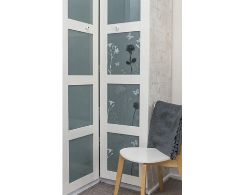 Weisser Schrank mit floralen Motiven und Glasfronten neben einem Stuhl mit einer grauen Decke