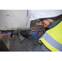 Un ouvrier du bâtiment, coiffé d''un casque de protection et vêtu d''un gilet de sécurité, utilise une scie sabre de marque Bosch pour couper un tuyau.