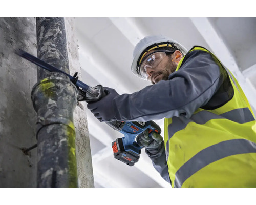 Un homme portant un casque de sécurité et des lunettes de protection scie un tuyau avec une scie sabre.