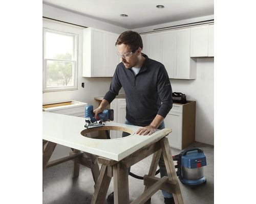 Un homme scie un trou dans un plan de travail dans une cuisine claire avec une scie sauteuse.