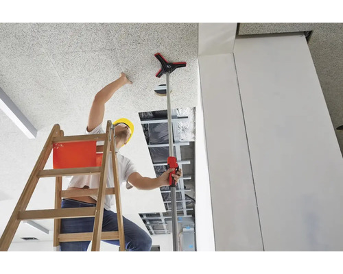 Ein Mann auf einer Leiter montiert eine Deckenplatte mit einem Montagewerkzeug.