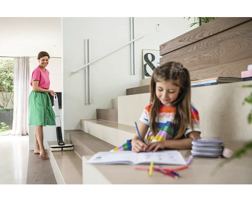 Une femme nettoie un escalier avec une serpillière électrique pendant qu''un enfant fait ses devoirs à côté