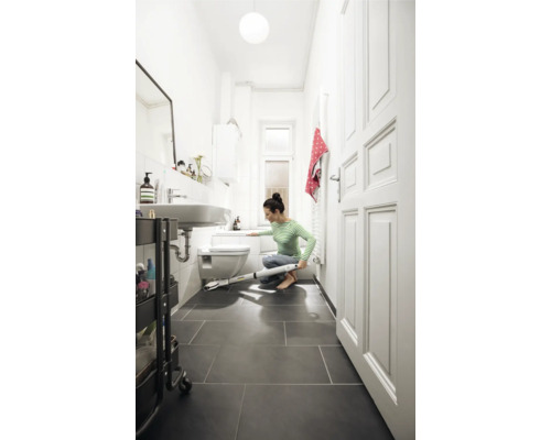 Une femme nettoie la salle de bains avec un nettoyeur de sol électrique.