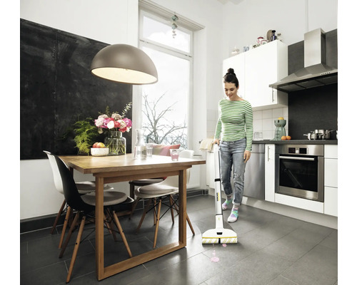 Une femme nettoie une cuisine avec coin repas à l''aide d''une serpillière électrique. La pièce est lumineuse et aménagée de manière moderne.