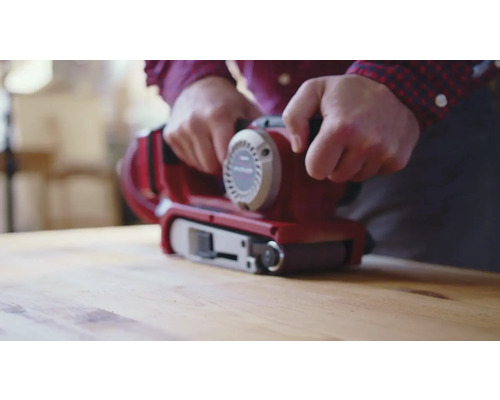Une personne utilise une ponceuse à bande sur une surface en bois.