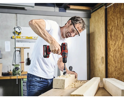 Un homme perce un morceau de bois avec une perceuse-visseuse sans fil dans un atelier.