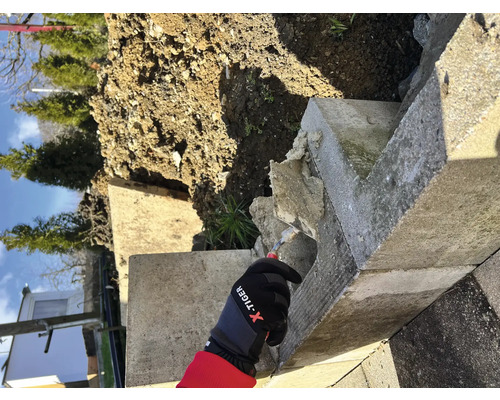 Ouvrier portant des gants effectuant des travaux de réparation sur un mur en béton dans le jardin.