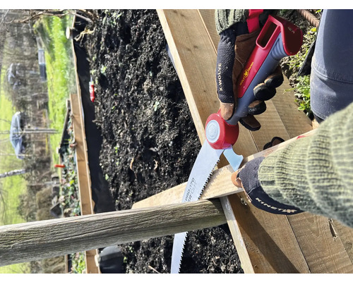 Person sägt Holzbrett mit einer Handsäge im Garten.