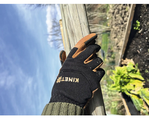 Eine Hand in einem Gartenhandschuh hält einen Holzpfosten.