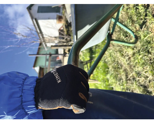 Nahaufnahme einer Hand mit Gartenhandschuh, die einen Schubkarren hält.