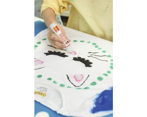 Eine Person bemalt ein T-Shirt mit einem Glitzerstift, um ein Katzengesicht zu gestalten.