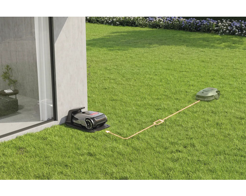 Szene mit einem Rasenmähroboter in der Ladestation und einem Rasenmähroboter auf dem Rasen