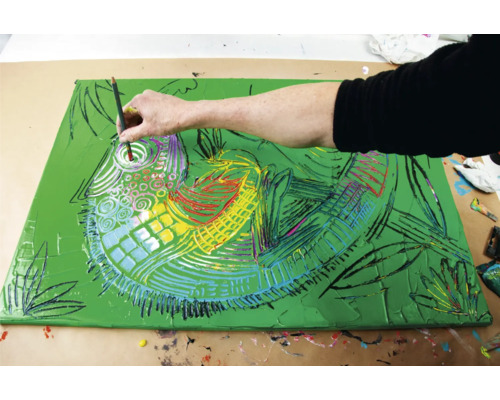 Un artiste peint un tableau sur toile avec un fond vert représentant un caméléon.