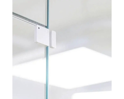 Weisser Fenster- oder Türkontaktsensor an einer Glasscheibe befestigt