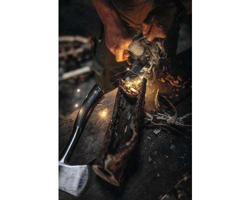 Un homme allume un feu dans une bûche avec un allume-feu, à côté d''une hache.