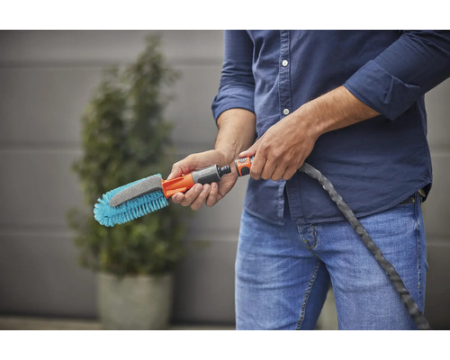 Eine Person hält eine Waschbürste mit Wasseranschluss.