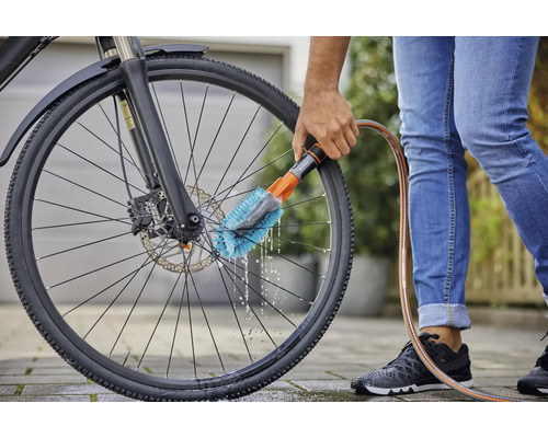 Eine Person reinigt ein Fahrradrad mit einer Bürste und einem Wasserschlauch