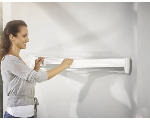 Une femme manipule un séchoir à linge mural blanc.