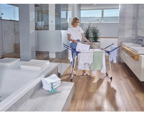 Femme étendant le linge sur un étendoir dans une salle de bain lumineuse.