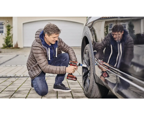 Mann wechselt mit einem Akku-Schlagschrauber ein Autorad