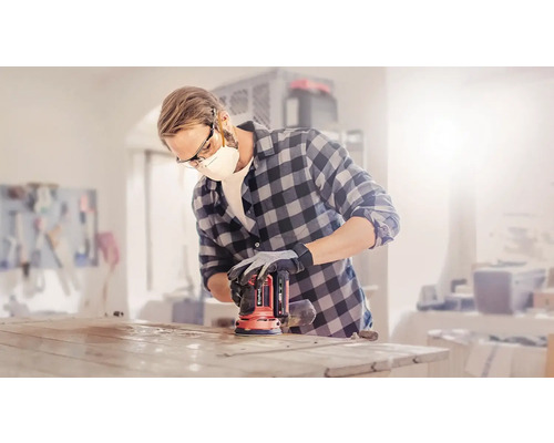 Un homme ponce un plateau de table avec une ponceuse excentrique