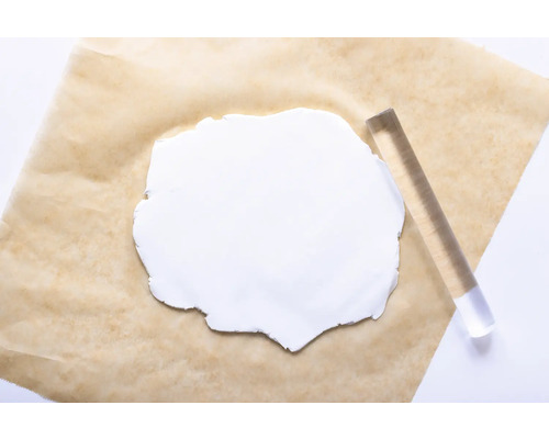 Un morceau de pâte à modeler blanche sur un papier sulfurisé avec un rouleau en acrylique.