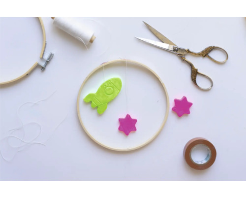 Scène de bricolage avec cadre à broder, fusée, étoiles, ciseaux et ruban adhésif