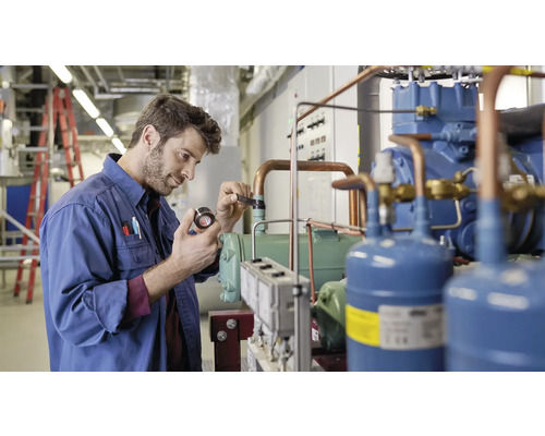 Ein Mann in Arbeitskleidung inspiziert ein Kühlaggregat in einem Technikraum.