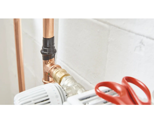 Les tuyaux de cuivre sont fixés au chauffage avec du ruban isolant noir et une vanne thermostatique.