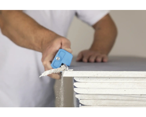 Un artisan ébavure une plaque de plâtre avec un ébavureur