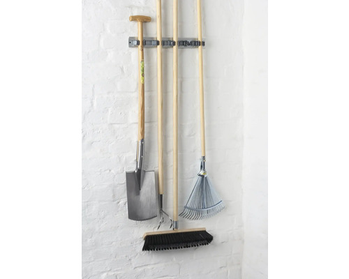 Outils de jardin tels que bêche, cultivateur, râteau et balai sur un porte-outils mural.