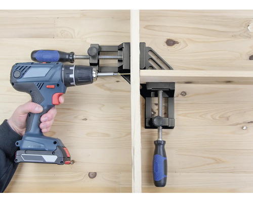 Une personne visse une pièce à l’aide d’une perceuse sans fil, qui est fixée avec une serre-joint d’angle.