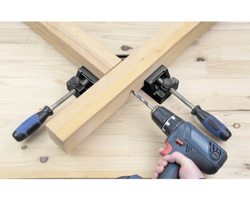 Une pièce est fixée avec une équerre de serrage et travaillée avec une visseuse sans fil.