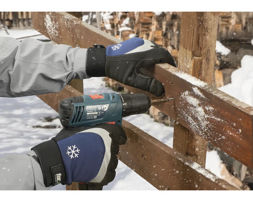 Une personne perce un trou dans une planche de bois avec une perceuse sans fil tout en portant des gants