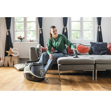 Eine Frau reinigt mit einem Waschsauger ein graues Sofa in einem Wohnzimmer.