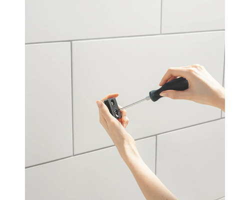 Une personne fixe un support à l''aide d''un tournevis devant un mur en carreaux blancs.