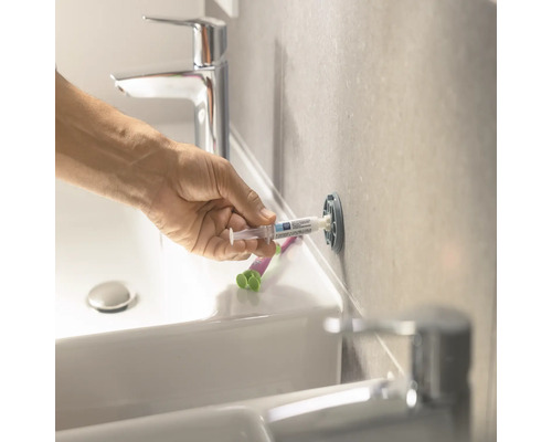 Personne réparant un trou de cheville dans la salle de bain avec du mastic de réparation