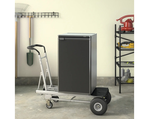 Réfrigérateur sur un chariot de transport dans un garage avec des outils de jardinage accrochés au mur